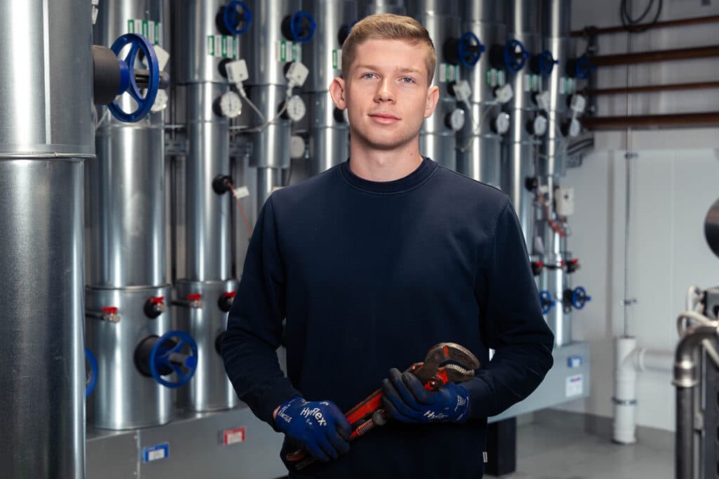 Young HVAC technician with pipe wrench in front of heating system